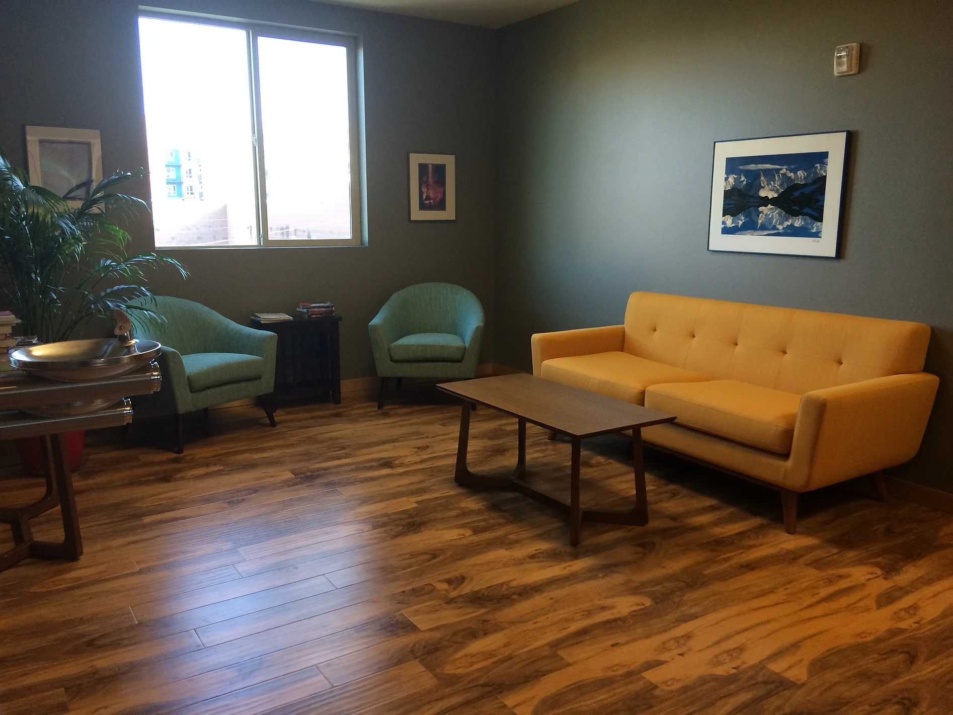 Picture of an open area with a window, two chairs, a couch, a small table, and two water fountains.